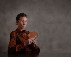 Photo of author Maude White. The author wears glasses and holds cards from the Pleasure Alchemy deck. She has a mysterious look on her face.